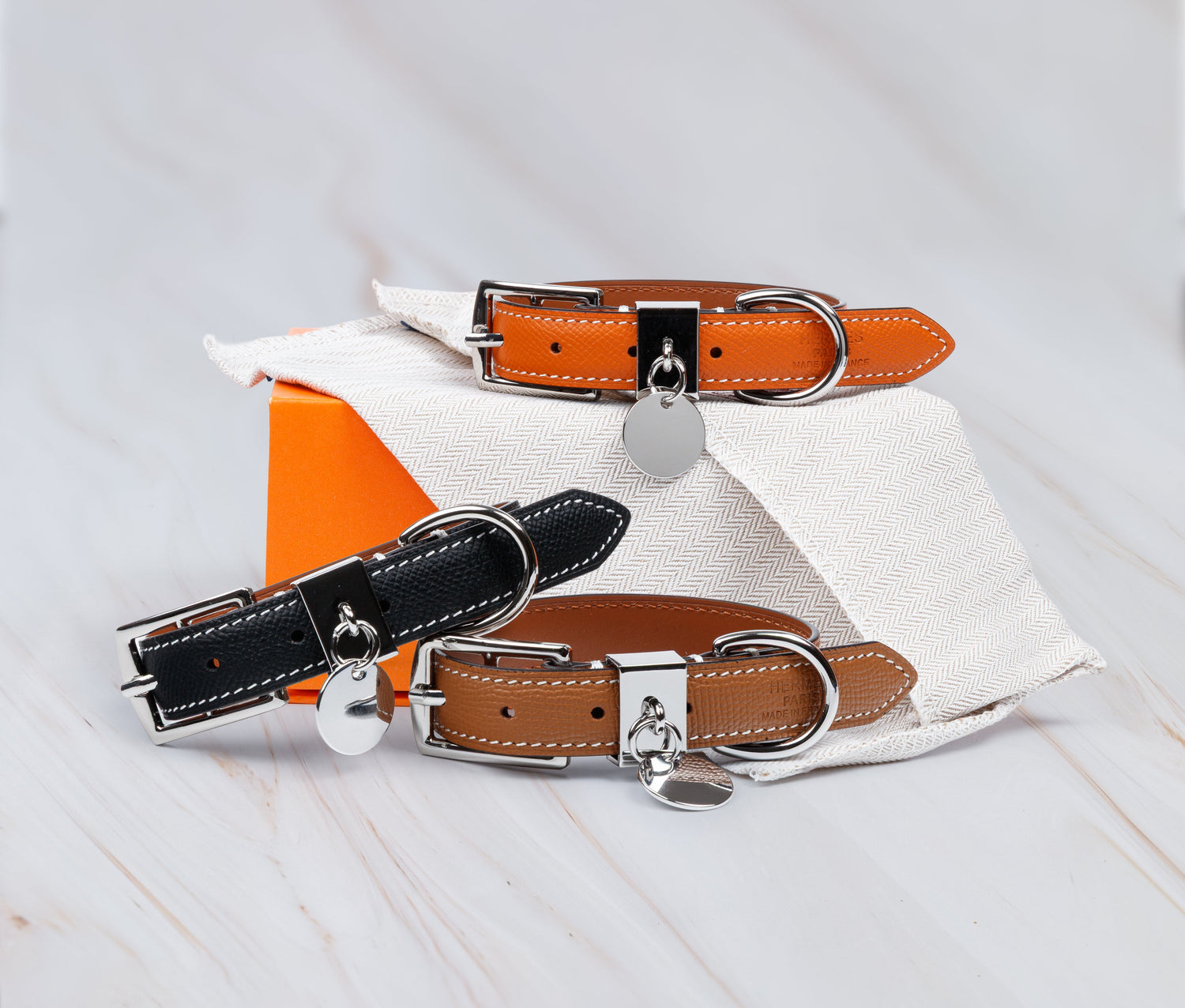 Three dog collars in black, brown, and orange on a white and orange fabric background.